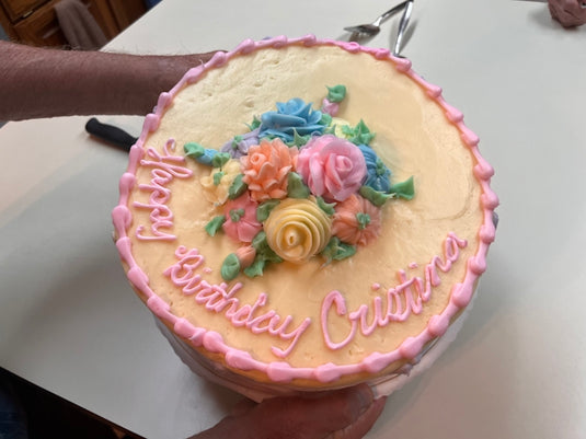 a person holding a birthday cake with flowers on it
