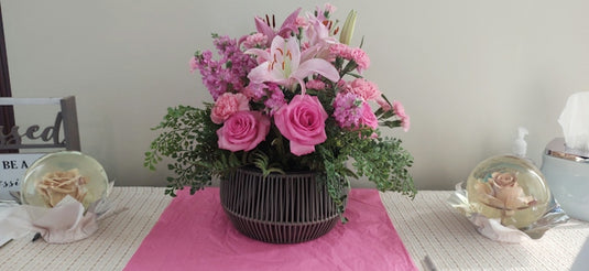 A floral arrangement of pink roses and lilies in a dark woven basket